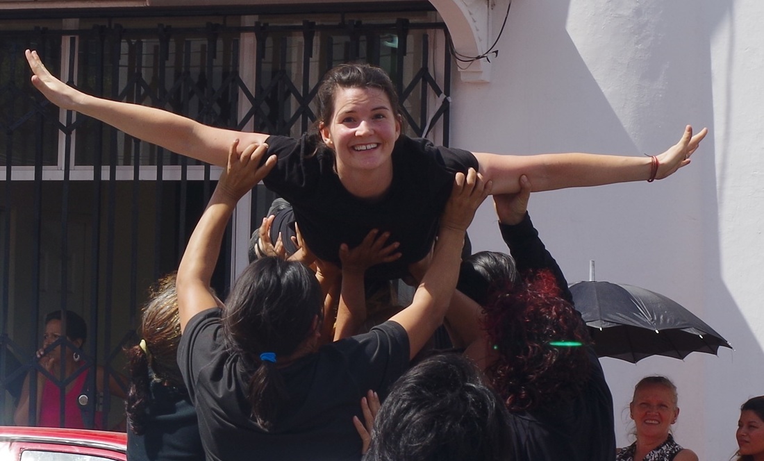 Sara smiling arms straight out to her side, with 7 women underneath her body lifting her up.