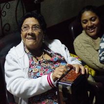 An 84 year old Nicaraguan woman holding a radio, looking up smiling.