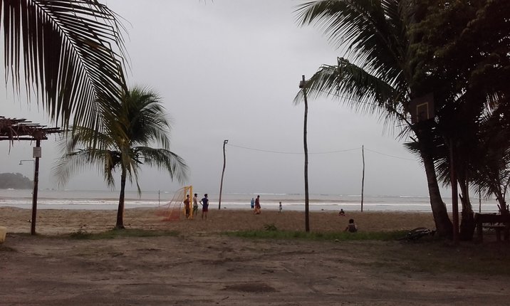 Picture of beach soccer game, barefoot players in the sand, grey sky, palm trees in foreground